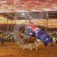 A man riding a horse carrying an Australian flag in a rodeo