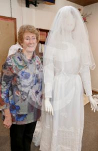 A elderly Lady standing next to an old wedding dress in the 100 year old uniting church in Grafton.