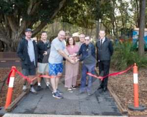 A group of people cutting a ribbon in the park at Lismore for a new path in the spine of Heritage Park.