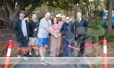 A group of people cutting a ribbon in the park at Lismore for a new path in the spine of Heritage Park.