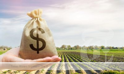 A hand holding a money bag in front of a field.