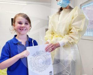 A dentist and school child holding an awrd in a dental van