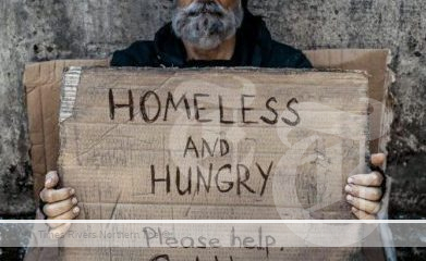 A homeless man with a sign on a street corner before erasing homelessness.