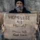 A homeless man with a sign on a street corner before erasing homelessness.