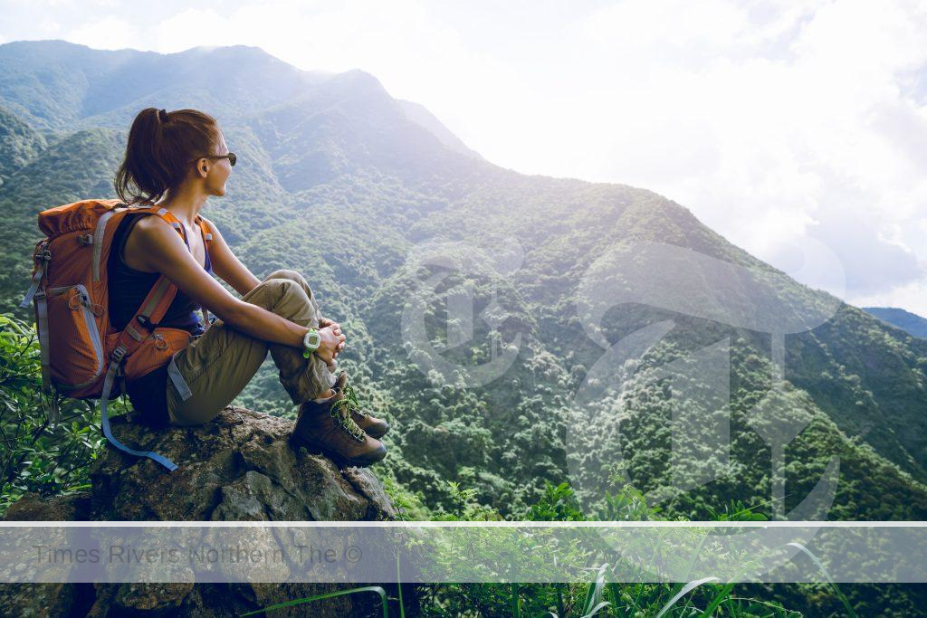 Young women first-time solo travellers sitting on a hill top.